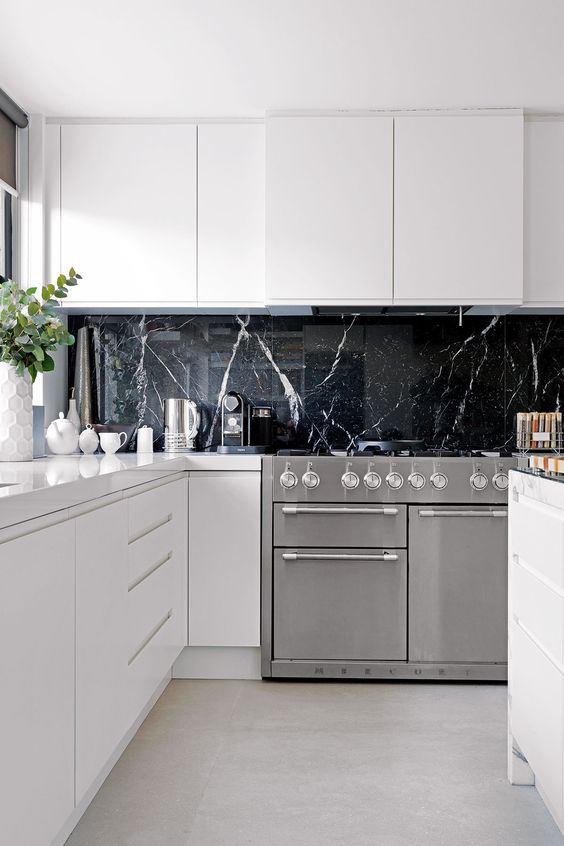 a black marble kitchen backsplash is a very luxurious touch to these ultra-minimalist white cabinets