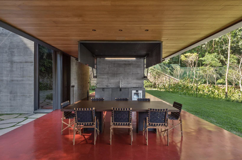 There's an outdoor kitchen done with metal and stone, and a dining space with a wooden table and leather chairs
