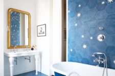 04 a bright bathroom clad with blue hexagon tiles and with stars printed on them, blue and white bathtub and a white free-standing sink