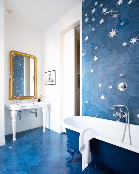 A bright bathroom clad with blue hexagon tiles and with stars printed on them, blue and white bathtub and a white free standing sink