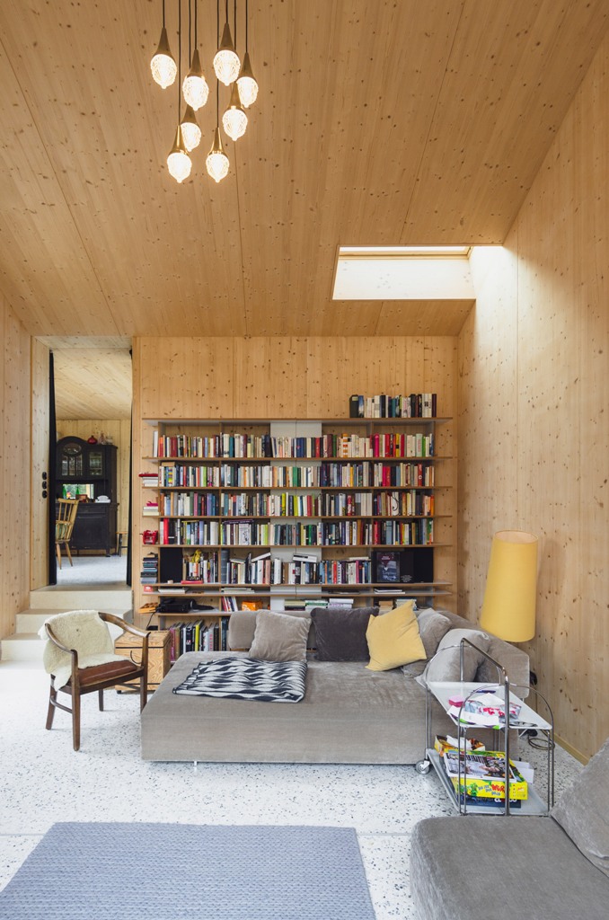 The living room is clad with light-colored wood, there are skylights and a wall of books