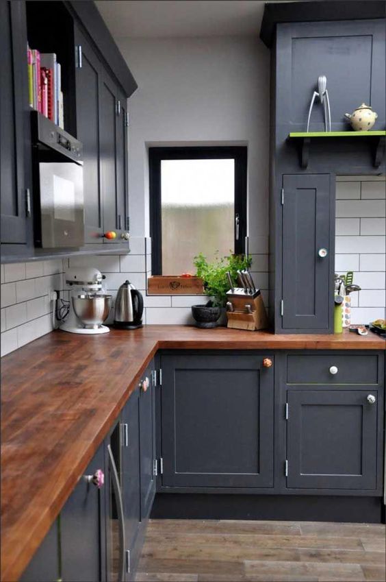a graphite grey kitchen with rich tone wooden countertops and a white tile backsplash