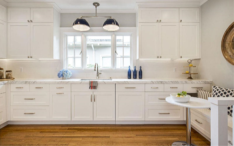 The kitchen is white, with a stone countertop and a small and cozy breakfast nook with a built-in seat