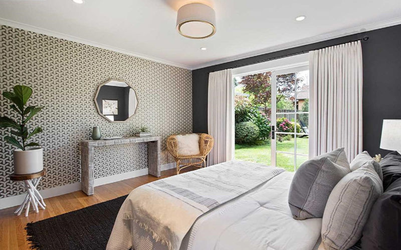 The bedroom is done with a printed wallpaper wall, a glass door to the garden and some stylish furniture