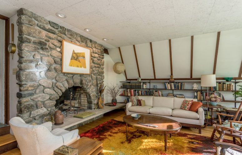 There's another living room with white walls, a stone fireplace and comfy mid-century modern furniture