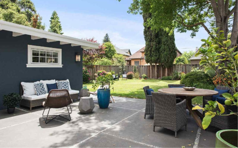 The backyard features a lawn and a dining and living space with stylish furniture and potted plants