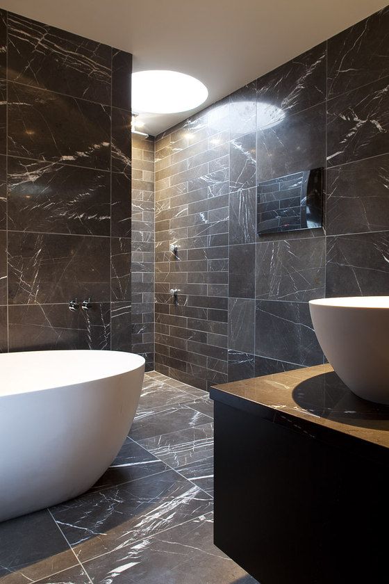 a chic minimalist bathroom clad with blakc marble tiles of various sizes and shapes plus white appliances for a contrast