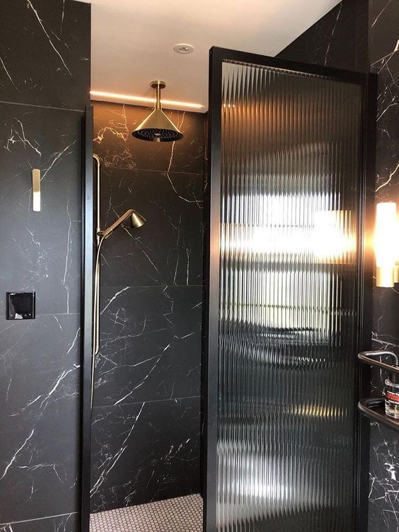 A refined modern bathroom clad with black marble tiles, with built in lights and matte black touches