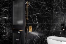 17 a stylish black bathroom clad with marble tiles, with a white tub for a contrast and brass touches