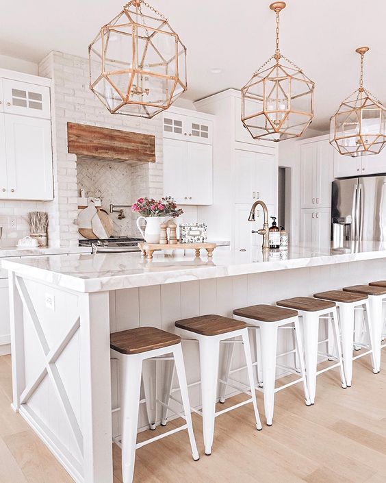 a white farmhouse kitchen with vintage gold faceted pendant lamps over the kitchen island