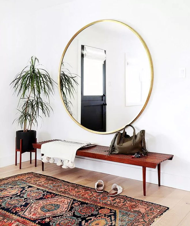 a boho chic entryway with a wooden bench, an oversized gold frame mirror, a boho rug and a potted plant