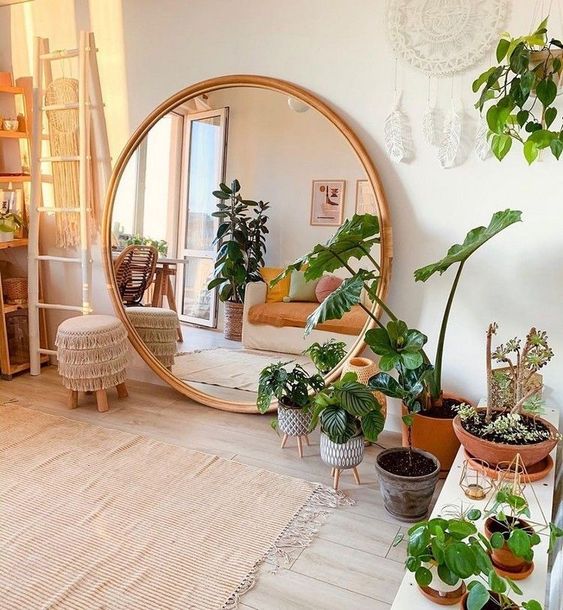 a boho chic living room in neutrals, with lots of potted greenery and an oversized round mirror