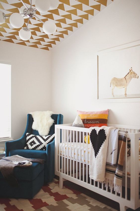 a boho kid's room with a gold geometric wallpaper ceiling, a graphic rug and pillow to make it bolder and cooler