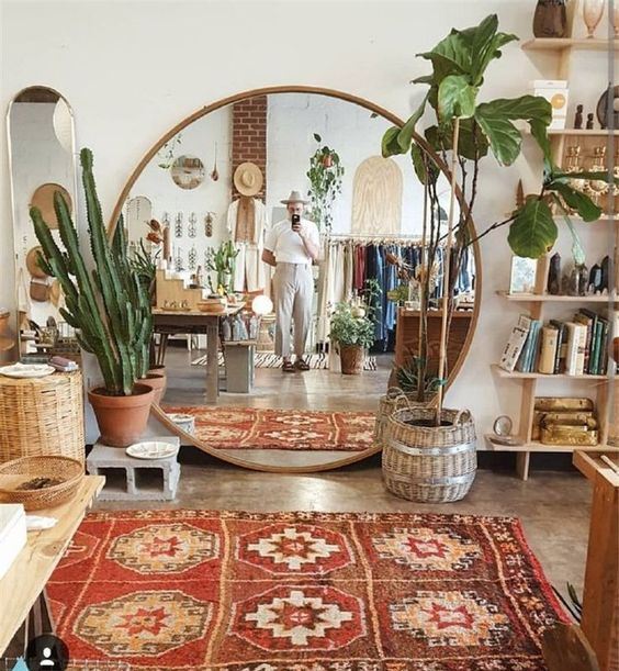 a boho living room with wooden and wicker furniture, potted plants, a boho rug and an oversized round mirror