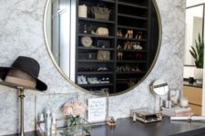 a chic closet with a makeup nook with a marble wall, a grey vanity, a gold frame mirror and many accessories