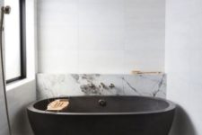 a chic contemporary bathroom with large scale tiles, white marble and concrete plus a black stone tub that wows