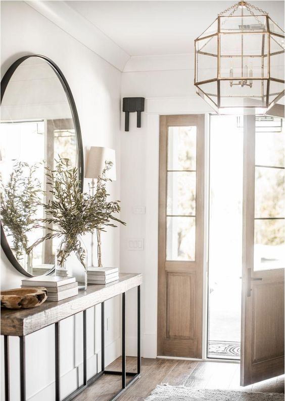a chic farmhouse entryway with a wooden and metal console, a catchy faceted chandelier and a round mirror