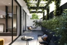 a chic modern patio with a long black planter along the wall, black garden furniture and much greenery climbing up the space