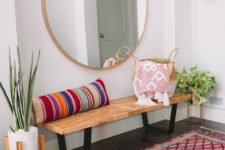 a colorful boho entryway with a wooden bench, a striped pillow, a round mirror, a bright rug and potted plants