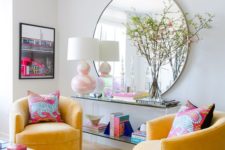 a colorful modern living room with neutral walls, yellow chairs, a slab table, an acrylic one and a round mirror