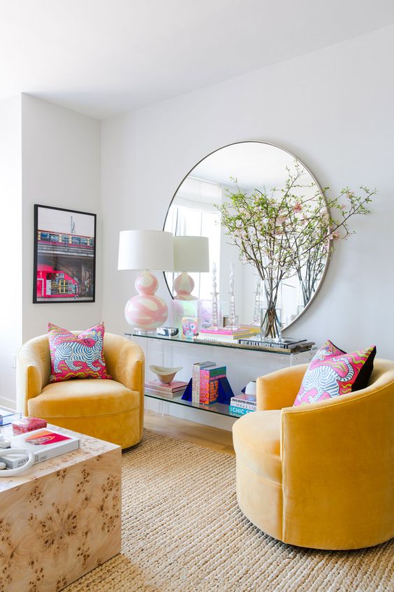 a colorful modern living room with neutral walls, yellow chairs, a slab table, an acrylic one and a round mirror