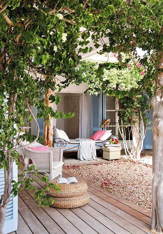 a cool backyard oasis with some trees, vines, a vintage daybed and rattan items plus pastel linens