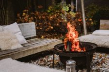 a fall backyard with wooden benches, faux fur, a fire pit and some pillows is super welcoming