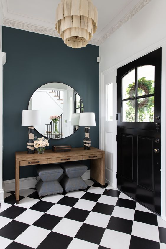 a glam art deco entryway with a wooden console table, grey stools, printed base lamps and a round mirror