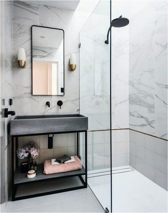 A glam bathroom clad with white marble, with tiles, a concrete sink and black fixtures to give it a fresher modern feel