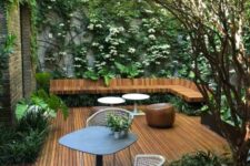 a gorgeous contemporary backyard with a wooden deck, a floating corner bench, a table and chairs and lots of greenery and blooms climbing up the wall