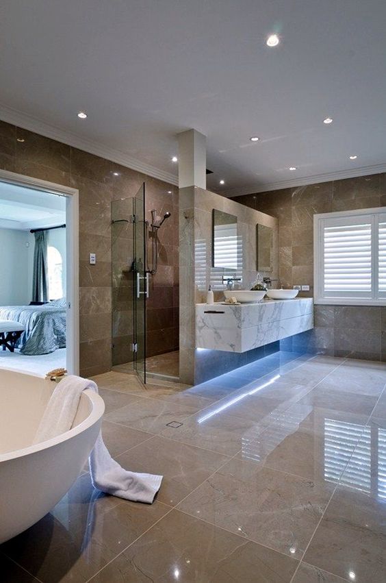 a large luxurious bathroom with tan and brown tiles, built-in lights, white appliances and a marble vanity