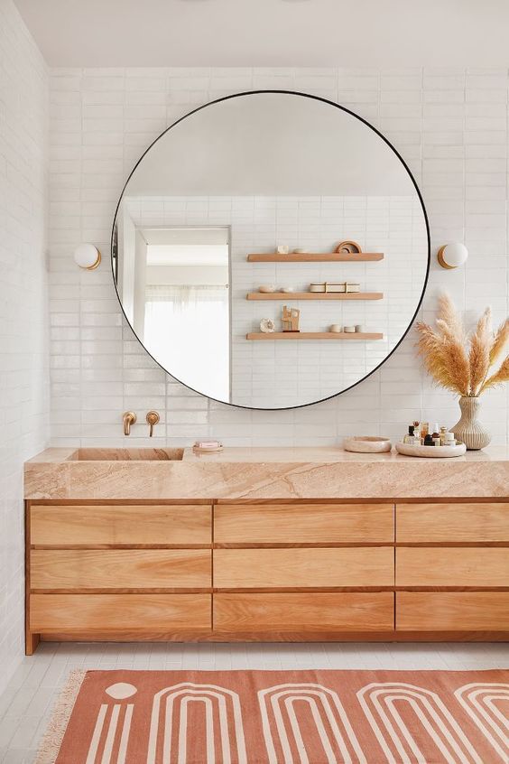 a modern natural bathroom with white tiles, a wooden vanity with a terracotta top and a large round mirror over it