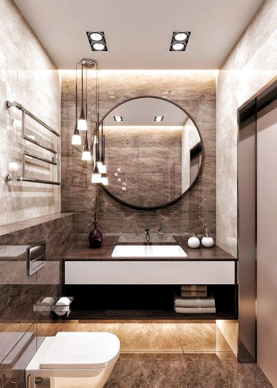 A refined brown bathroom with tiles, built in lights, pendant lamps and a round mirror