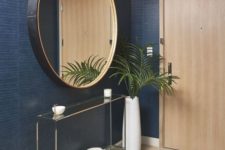 a refined modern foyer with navy walls, a glass console, a black frame round mirror and a plant in a vase