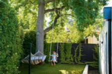 a small and dreamy backyard with living walls, a large tree, grass, a hammock and a swing, with a wooden deck