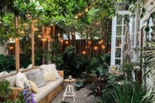 a small and welcoming backyard with a sofa, potted plants and blooms, climbing plants over the space and lights