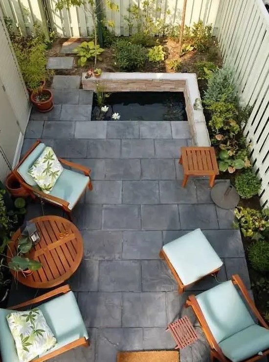 a small and zen-like backyard with tiles on the ground, a tiny pond, some growing plants and cool garden furniture with blue upholstery
