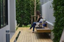 a small modern backyard with a deck and a floating bench plus greenery walls and a tree for relaxing outside