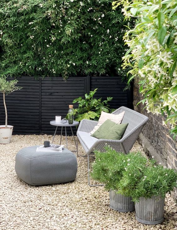 a small modern backyard with gravel on the ground, with rattan furniture and potted plants and blooms