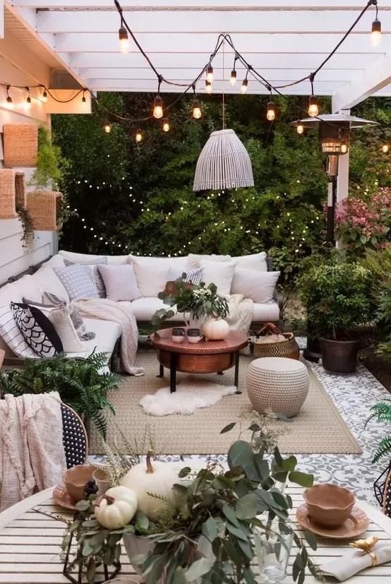 A small outdoor space with an L shaped sofa, lights and lanterns, a chair, a copper coffee table and some ottomans