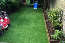 a small walled backyard turned into a kids’ entertainment zone with a kid house, some cars and other stuff and covered with artificial turf