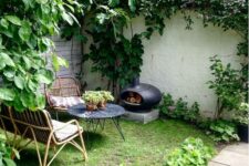 a small yet cozy backyard with rattan furniture, a marble top table, a little hearth and a green lawn