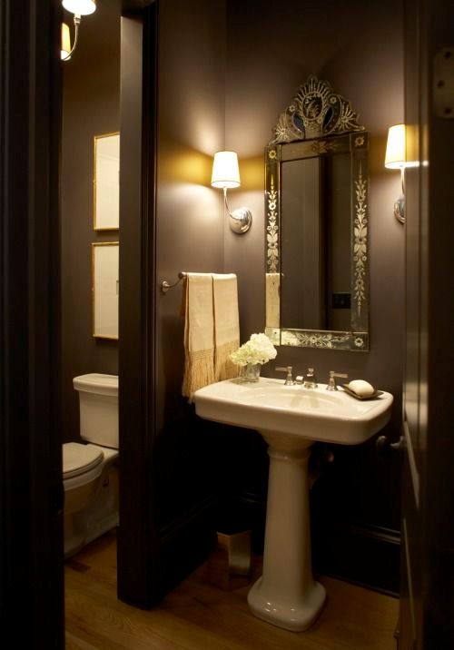 A stylish brown bathroom with a vintage mirror, a free standing sink and vintage fixtures and lights