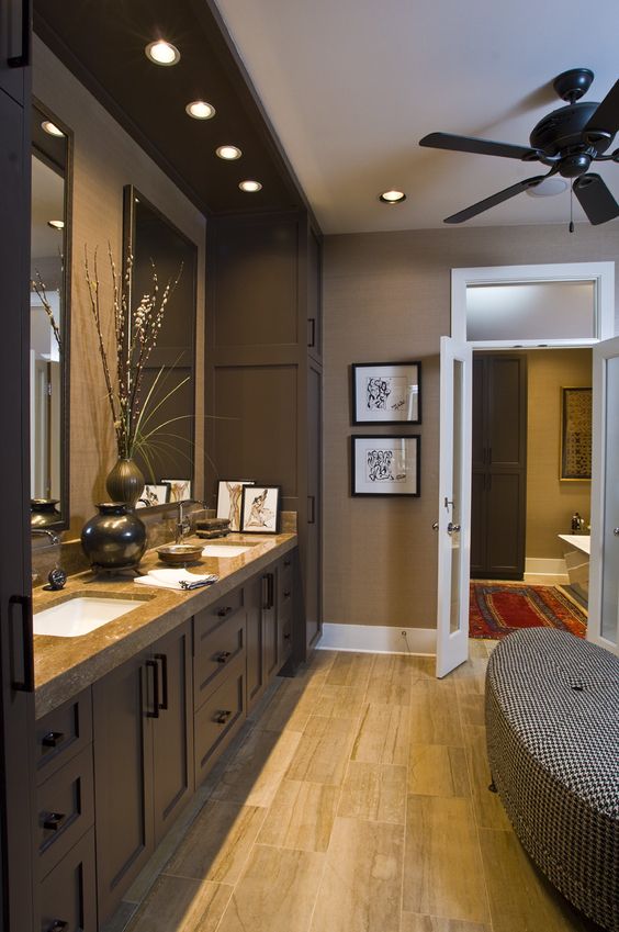 a stylish brown bathroom with tan walls, chocolate brown furniture, a stone countertop and a printed upholstered bench