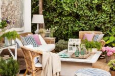 an outdoor living room with rattan furniture, a coffee table, printed pillows and poufs, potted plants and greenery