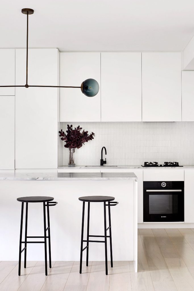 The kitchen is done in white, with white stone countertops, a catchy lamp and black stools