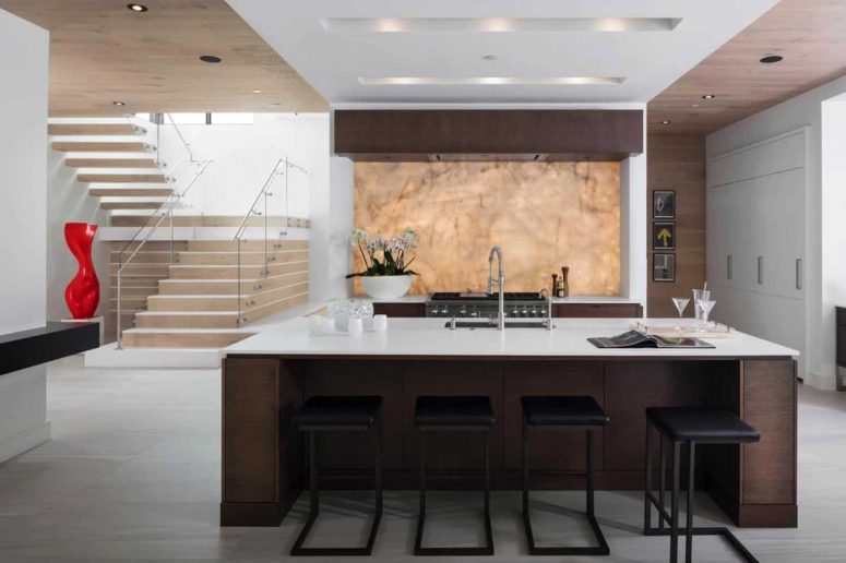 The kitchen is done with dark stained furniture, white stone countertops and a gorgeous quartzite backlit backsplash