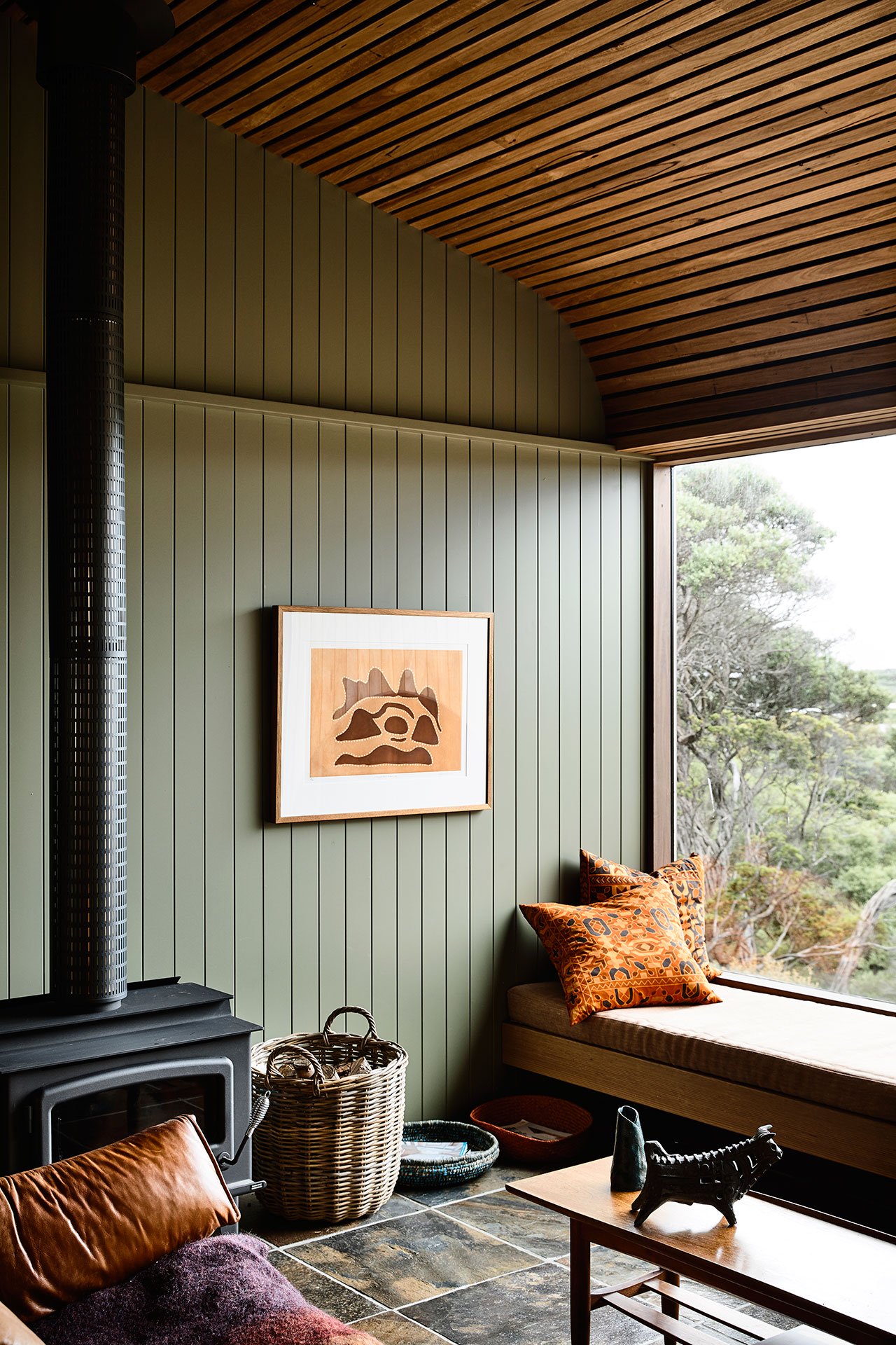 The living room features a wood slab ceiling, sage green wooden walls and a comfy window seat plus a hearth