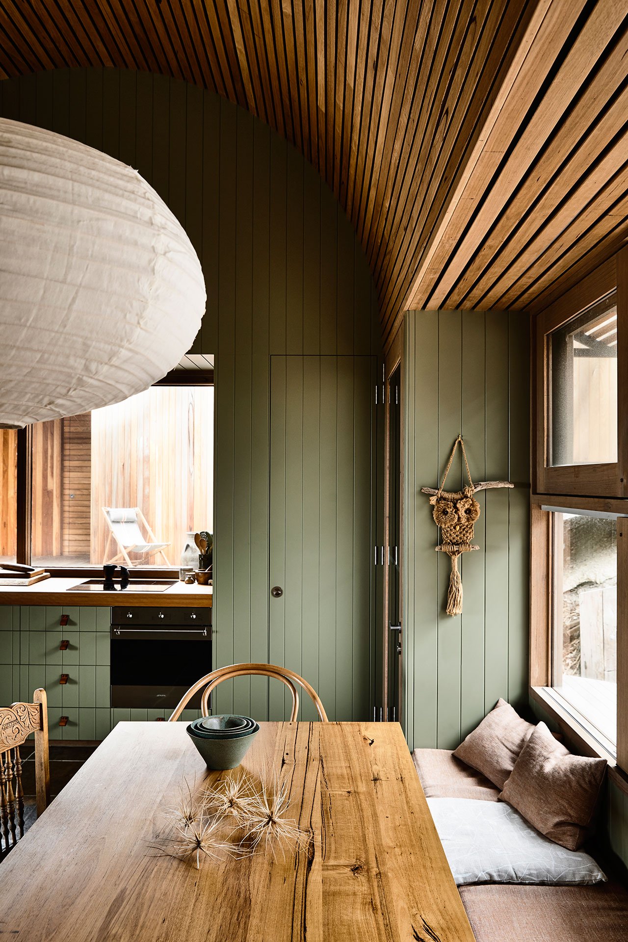 The kitchen and dining room are united into one space also clad with sage green wood and with matching furniture
