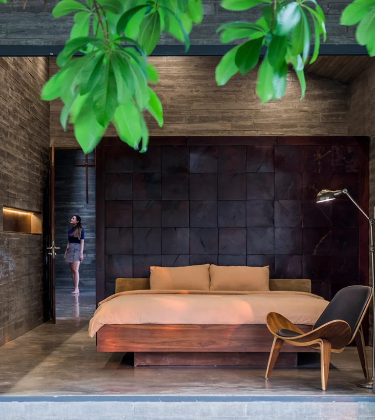 The bedroom shows off woodgrain concrete boards, a gorgeous wood stained wall and chic wooden furniture